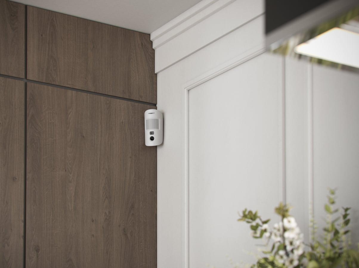 Détecteur Ajax MotionCam fixé près d’une porte dans un intérieur
